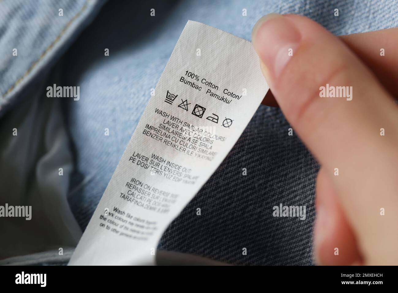 Woman reading clothing label with care symbols and material content on jeans, closeup Stock