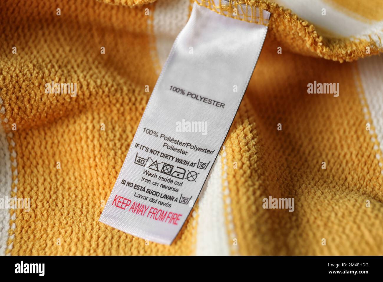 Clothing label with care symbols and material content on yellow shirt, closeup view Stock Photo