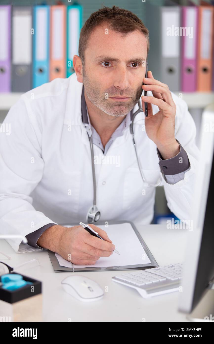 male doctor using telephone while working on computer Stock Photo