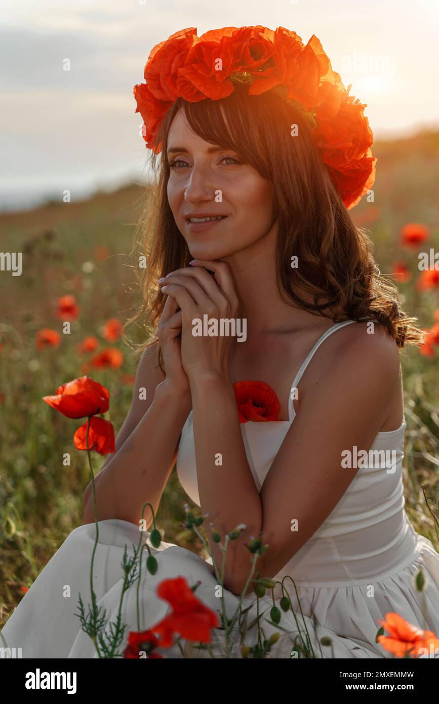 A beautiful young woman in a white dress with a wreath of poppies on ...