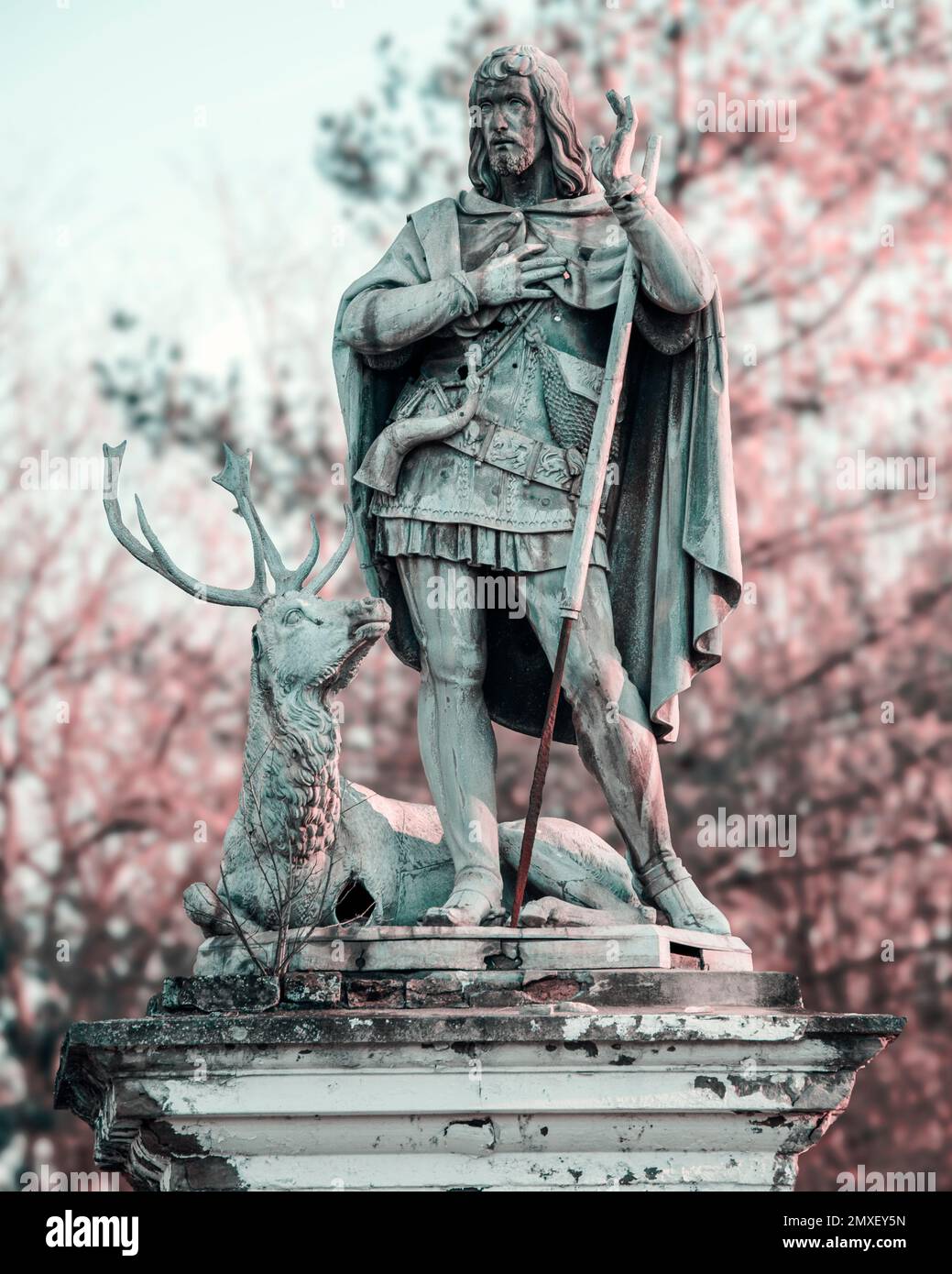 A vertical shot of the statue of St. Hubert against blooming trees in