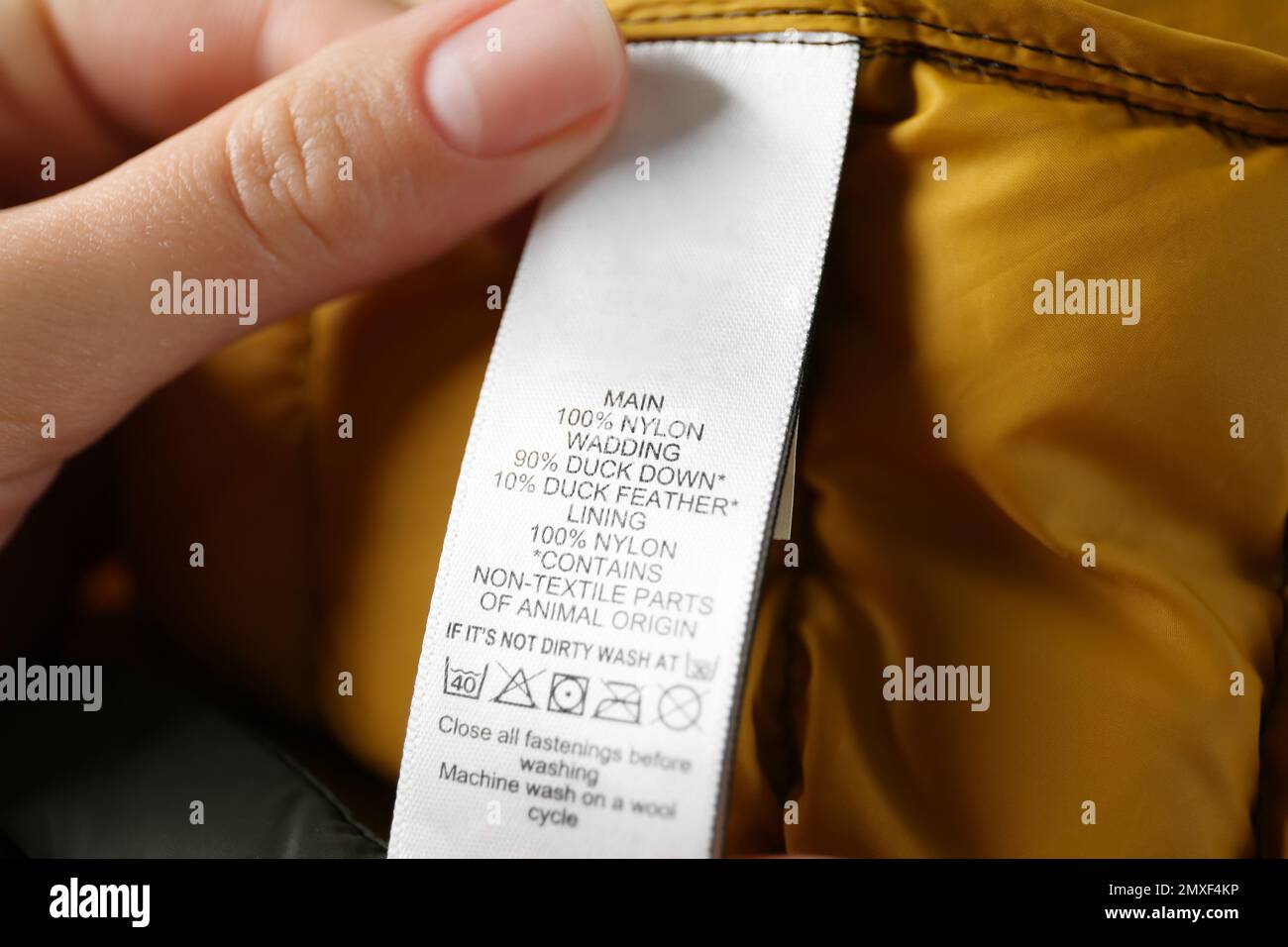 Woman reading clothing label with care symbols and material content on color jacket, closeup