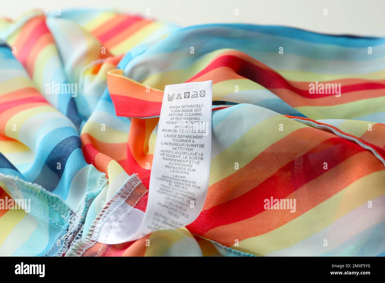 Clothing label with care instructions on colorful striped garment, closeup Stock Photo