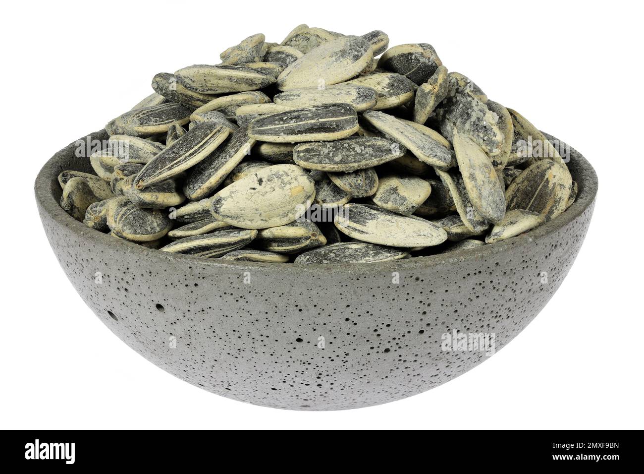 whole roasted and salted sunflower seeds in a concrete bowl isolated on white background Stock Photo