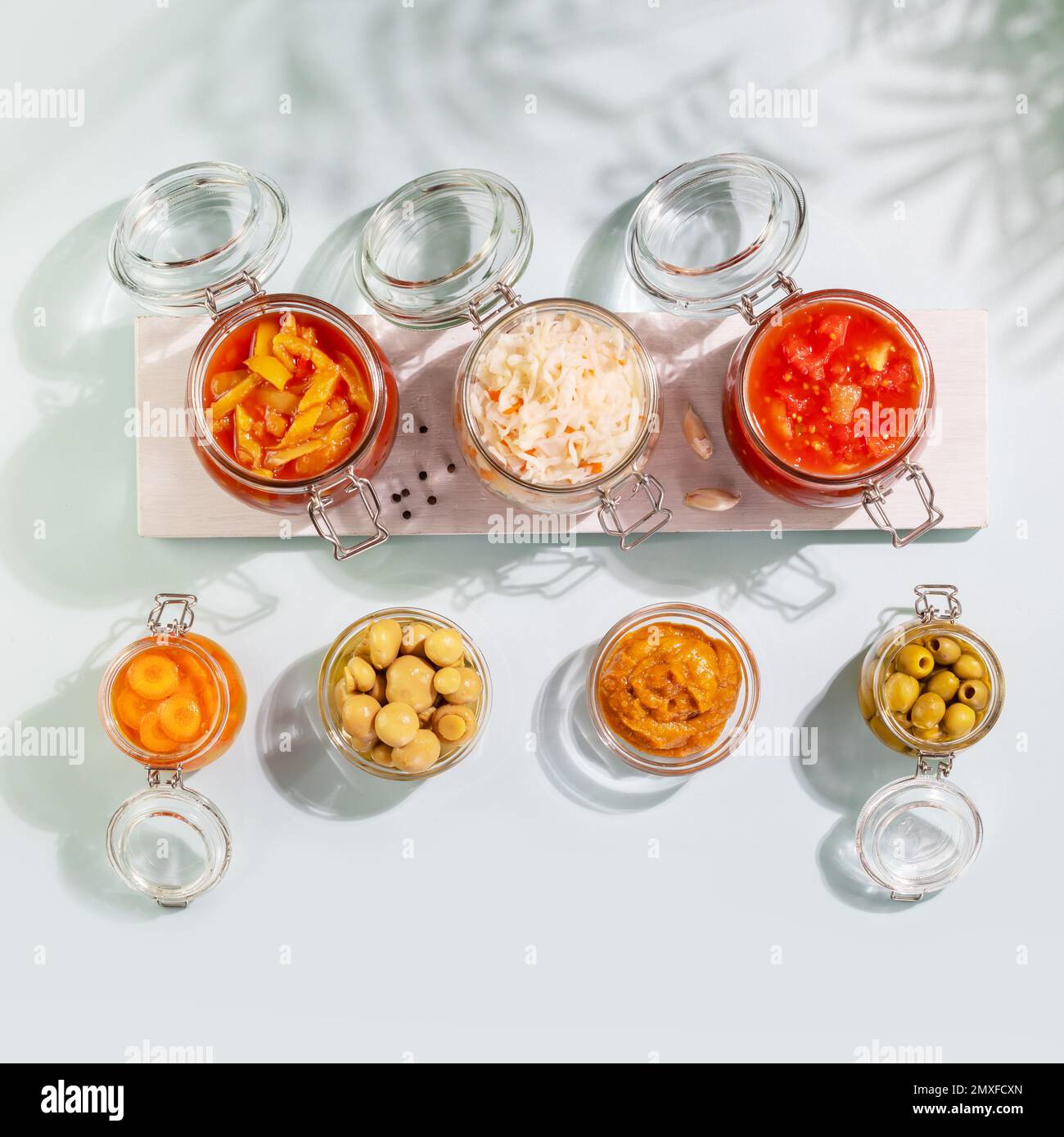 Probiotic foods. Pickled or fermented vegetables and mushrooms in glass jars on white wooden board on blue background with shadows. Home food preservi Stock Photo