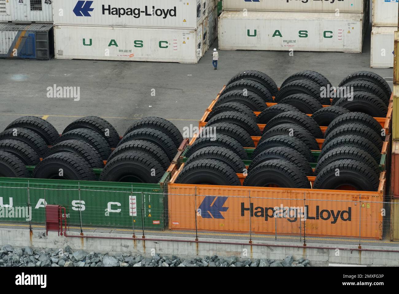 Orange and green containers loaded with big tires for heavy goods lorry or trucks situated on container terminal. Stock Photo