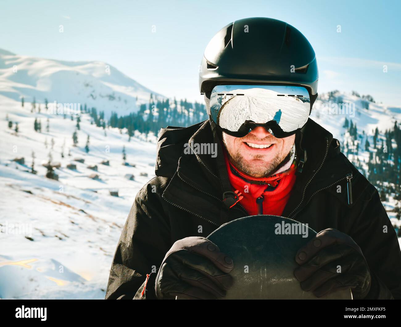 Close up portrait caucasian man with the reflection of snowed mountains, white slope and ski resort. A mountain range reflected in the ski mask. Portr Stock Photo