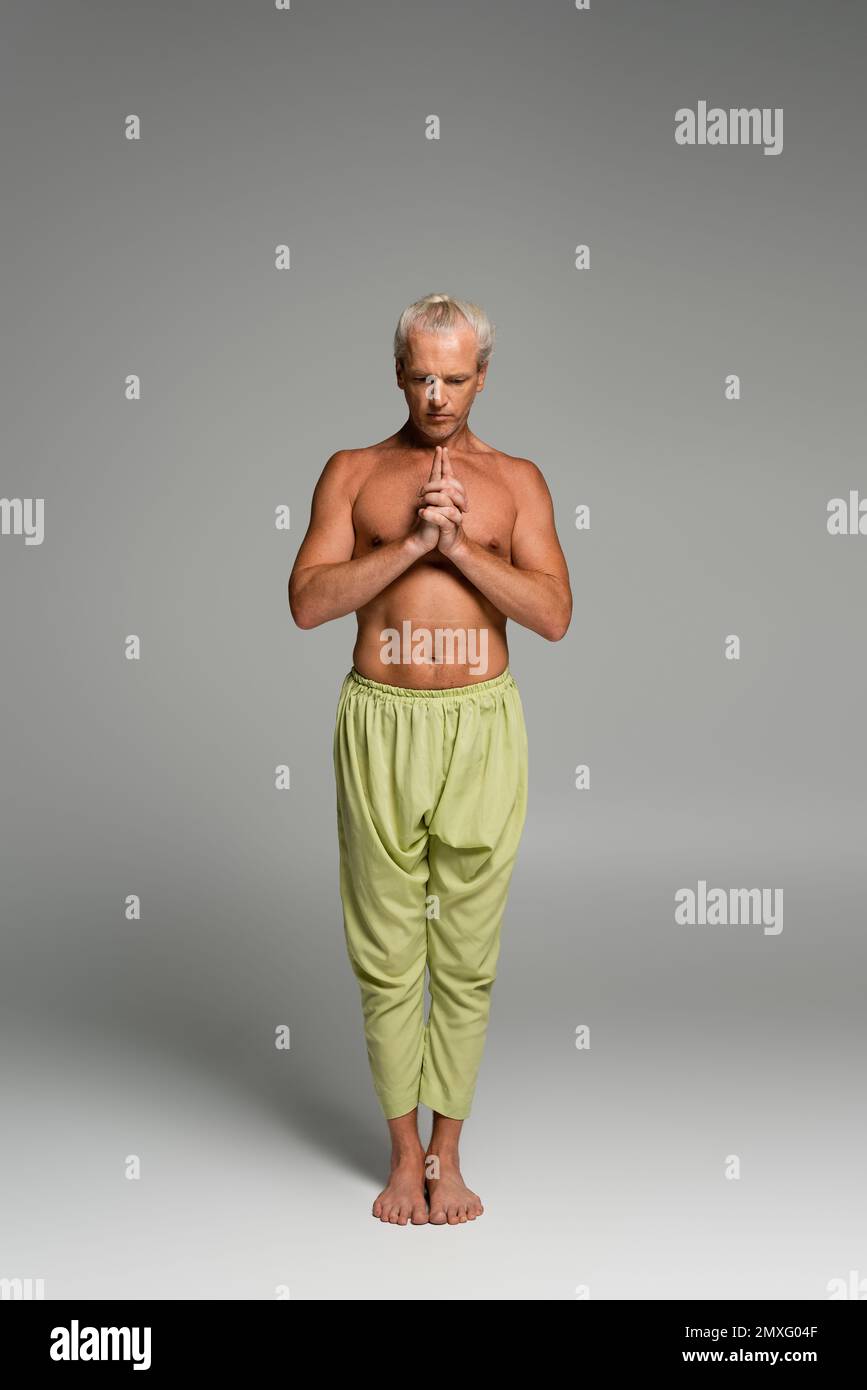 full length of barefoot man in pants meditating while doing kali mudra on grey,stock image Stock Photo