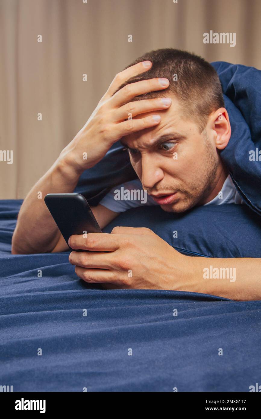 Upset confused young man holding mobile phone, having mobile phone problems or missed call, frustrated angry student reading bad news in message, look Stock Photo