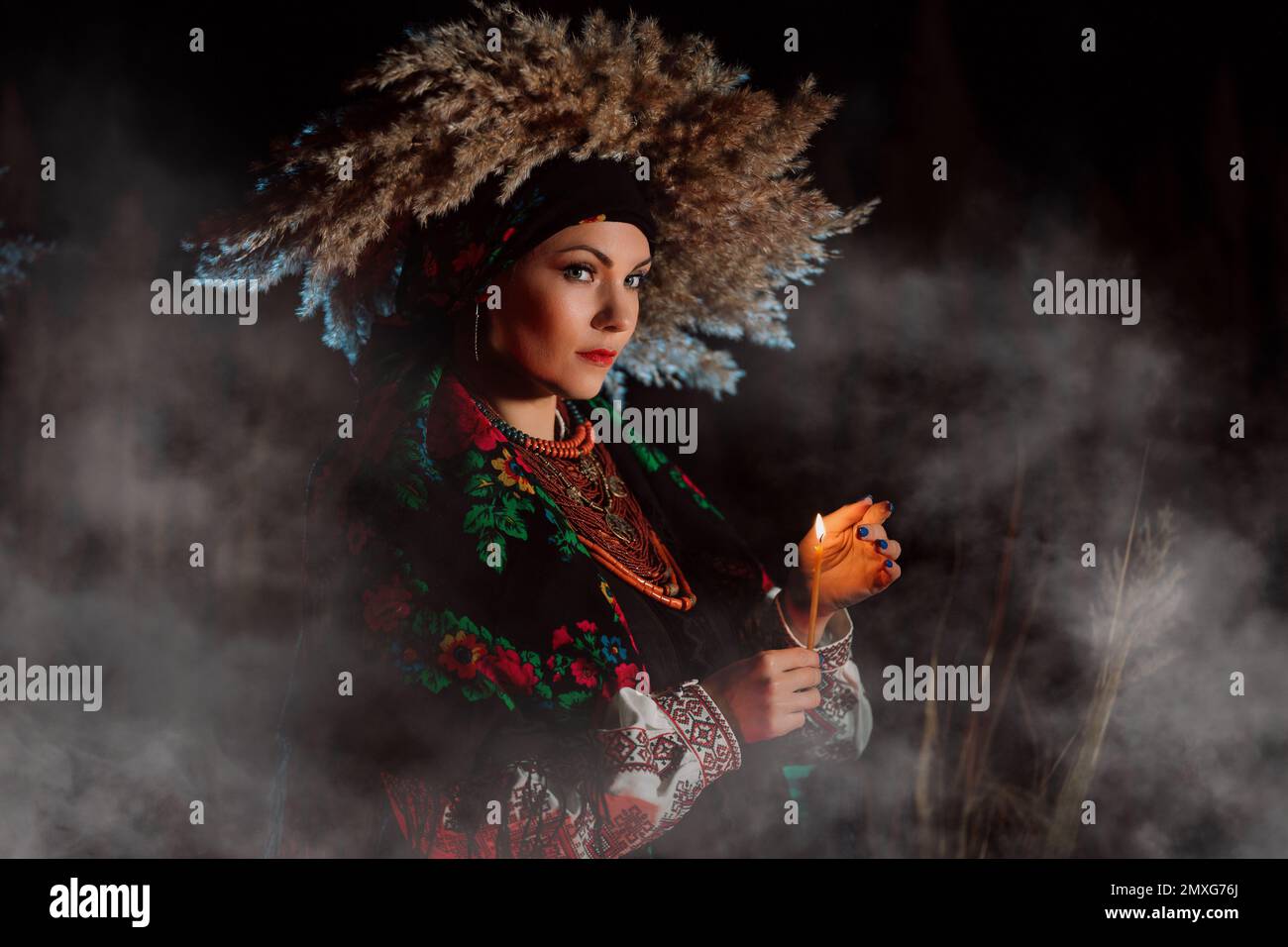 Mysterious ukrainian woman with candle, she in traditional costume outdoors at night. Lady in authentic jewelry. Beauty of Ukraine, ethnic clothing, d Stock Photo