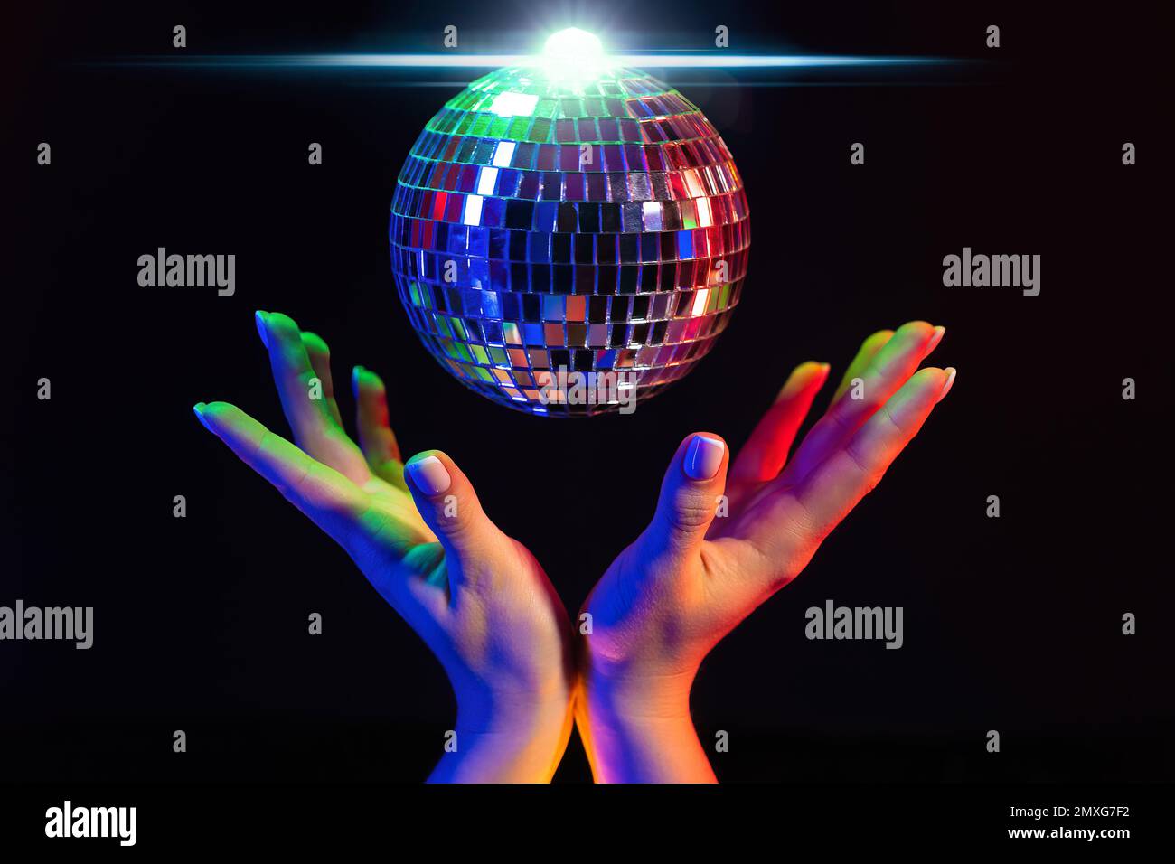 Female hand holding spinning disco mirror ball under neon. Glossy silver sphere reflecting light. Retro night party, music and entertainment concept b Stock Photo