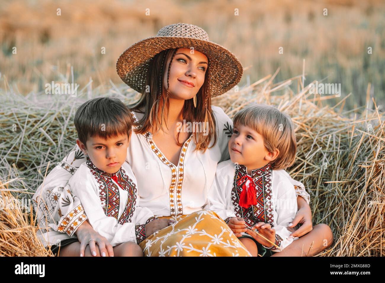 Beautiful ukrainian family - woman and sons in vyshyvanka shirts lying on hay in countryside at sunset. Nature, haystack, vacation, relax and harvest Stock Photo