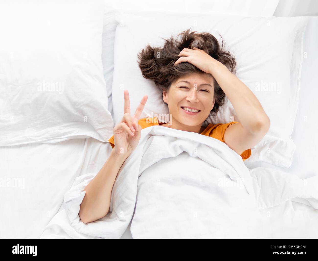 Top view on sleepy woman showing Victory gesture in bed. Woman