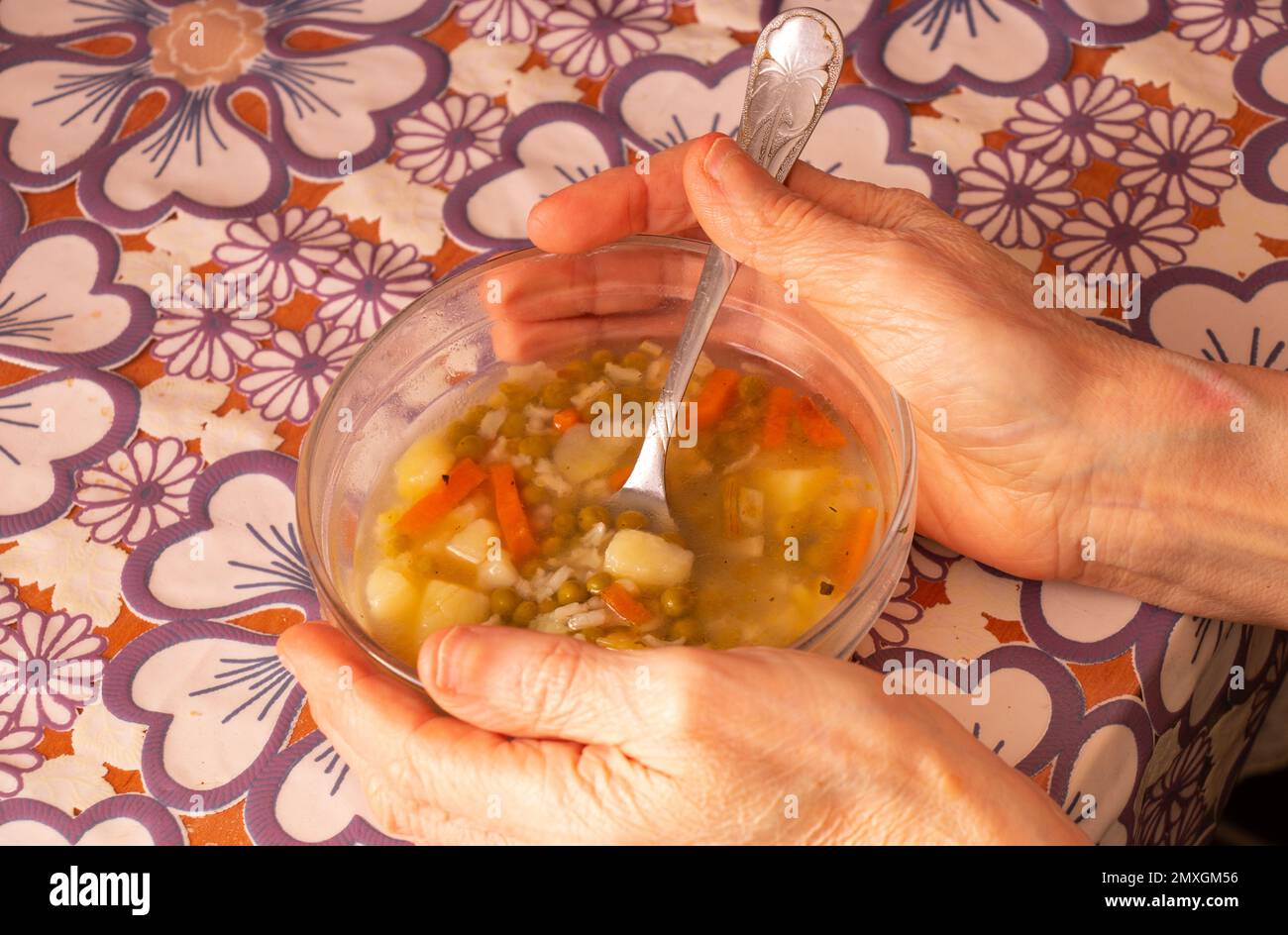 elderly woman holding a bowl of soup at the table in the kitchen Stock