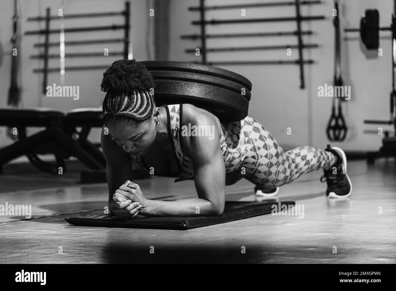 Woman training in modern light studio. Doing a plank with weight on your back. Flexion on weights. Stock Photo