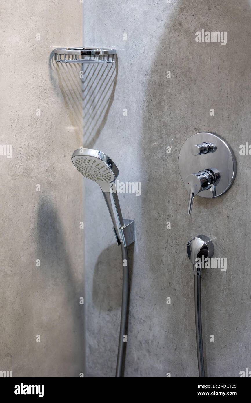 A shower head mounted to the wall of a shower tray finished with gray ceramic tiles. Next to the shelf to hold the soap Stock Photo
