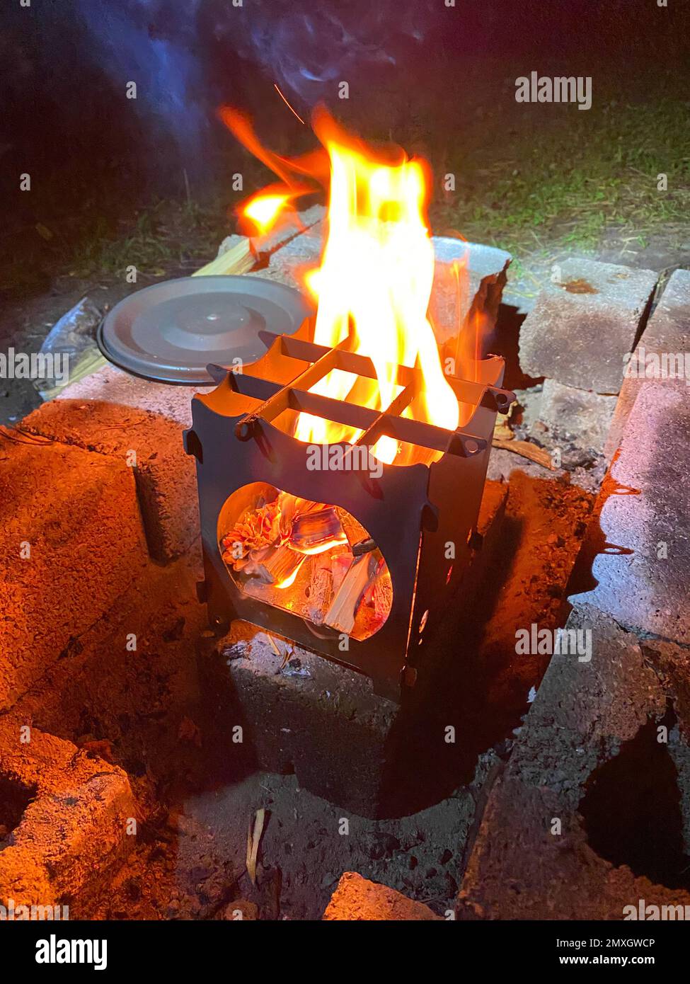 The wood burning burner burns at night next to the pot lid Stock Photo