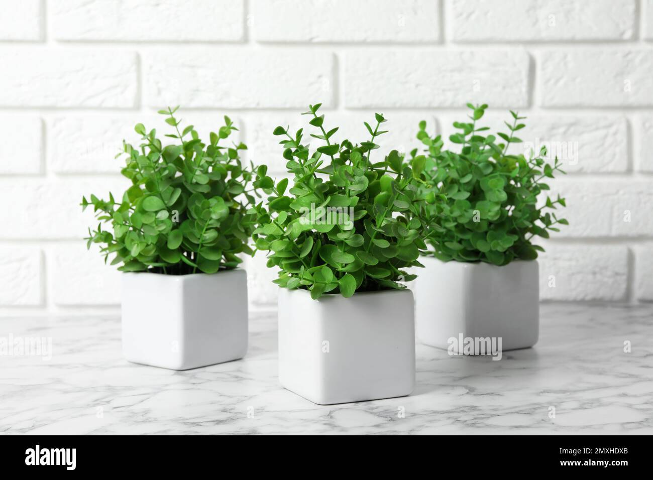 Beautiful artificial plants in flower pots on white marble table near brick wall Stock Photo