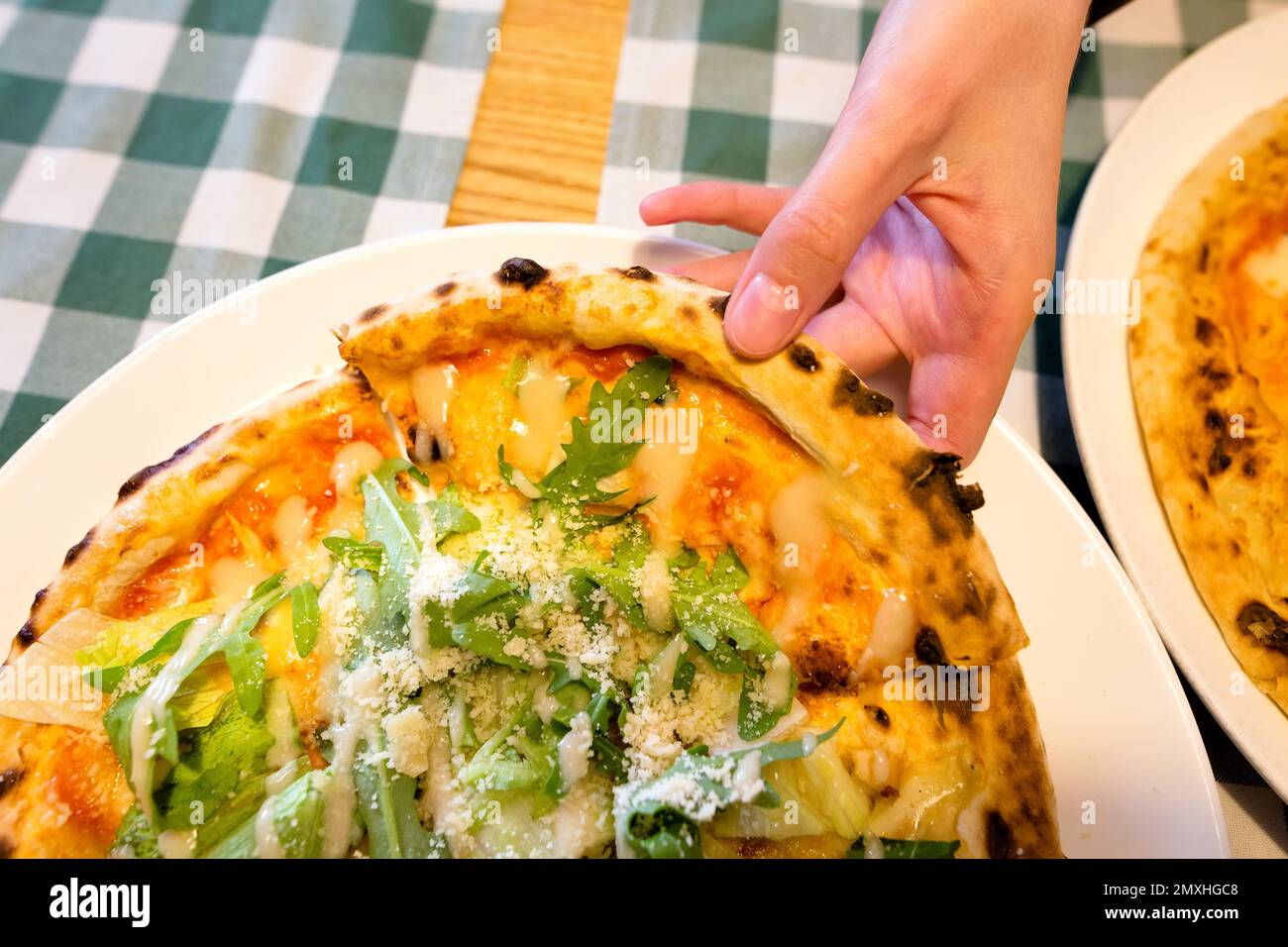 Female hands taking slices of authentic Italian caesar stone oven pizza with arugula, sauce, grilled chicken, herbs and spicy parmesan cheese. Stock Photo