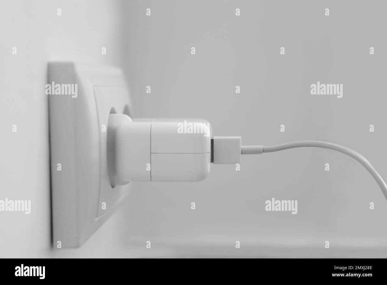 Charging adapter plugged in electric socket, closeup Stock Photo