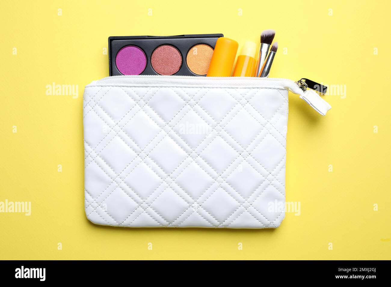 Bag with hygienic lipsticks and cosmetic products on yellow background