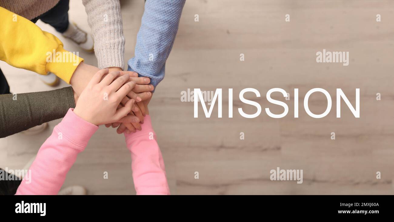 People holding hands together over wooden background and text MISSION ...