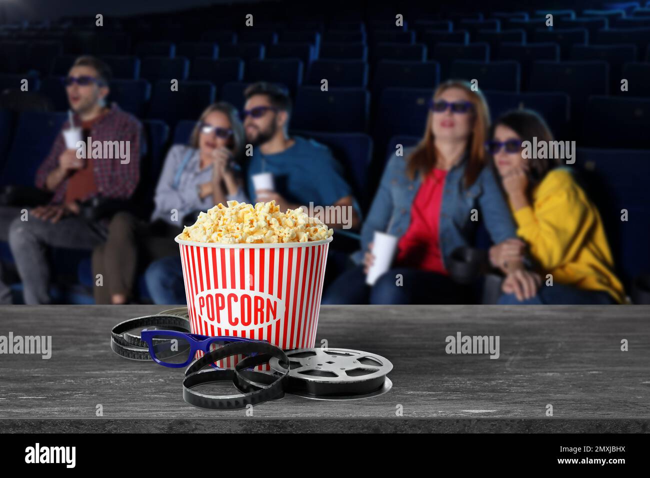 Popcorn, 3D glasses, movie reel on table and young people in cinema hall Stock Photo