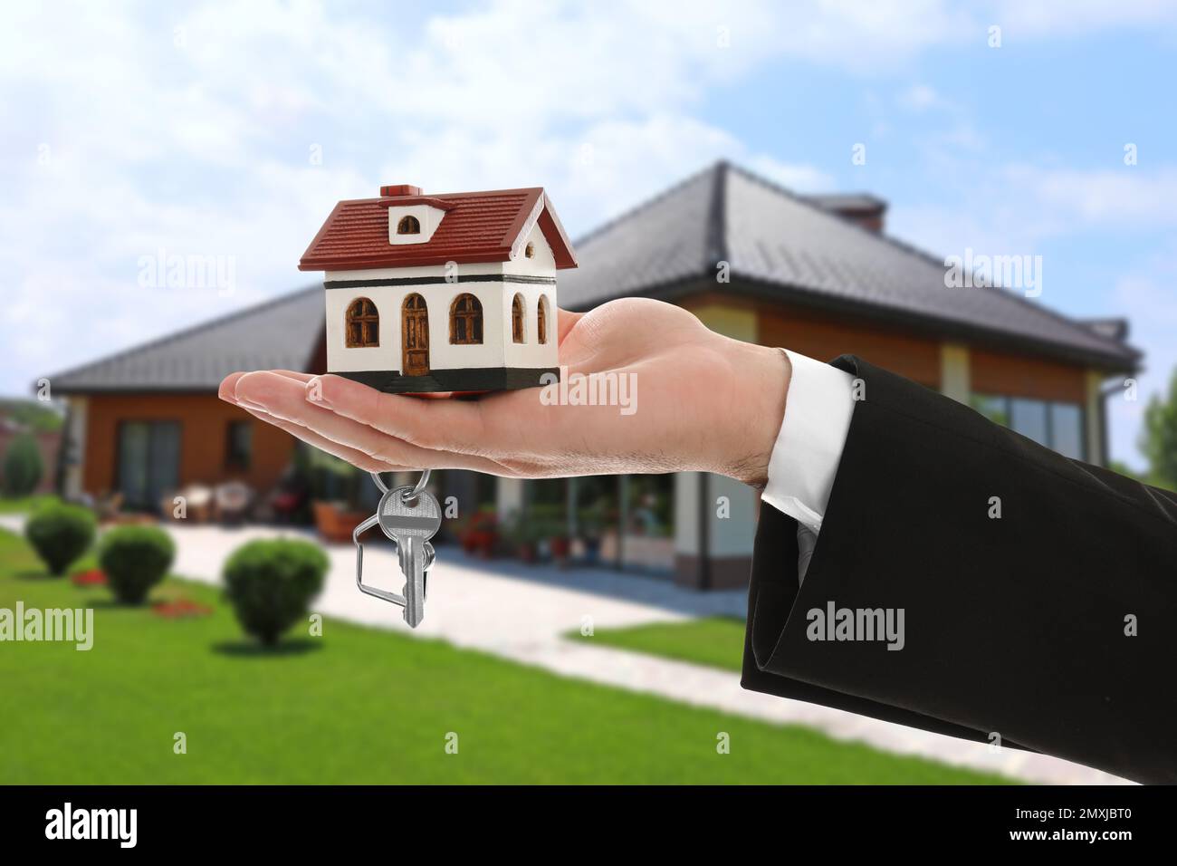 Real estate agent holding key and house model against beautiful villa ...