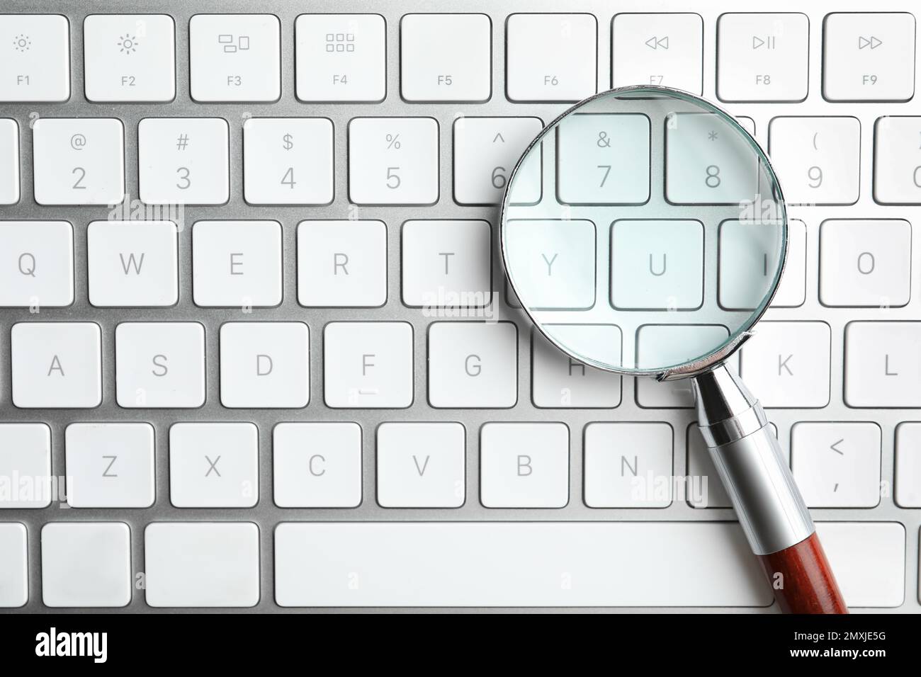 Magnifier glass on modern keyboard, top view. Find keywords concept
