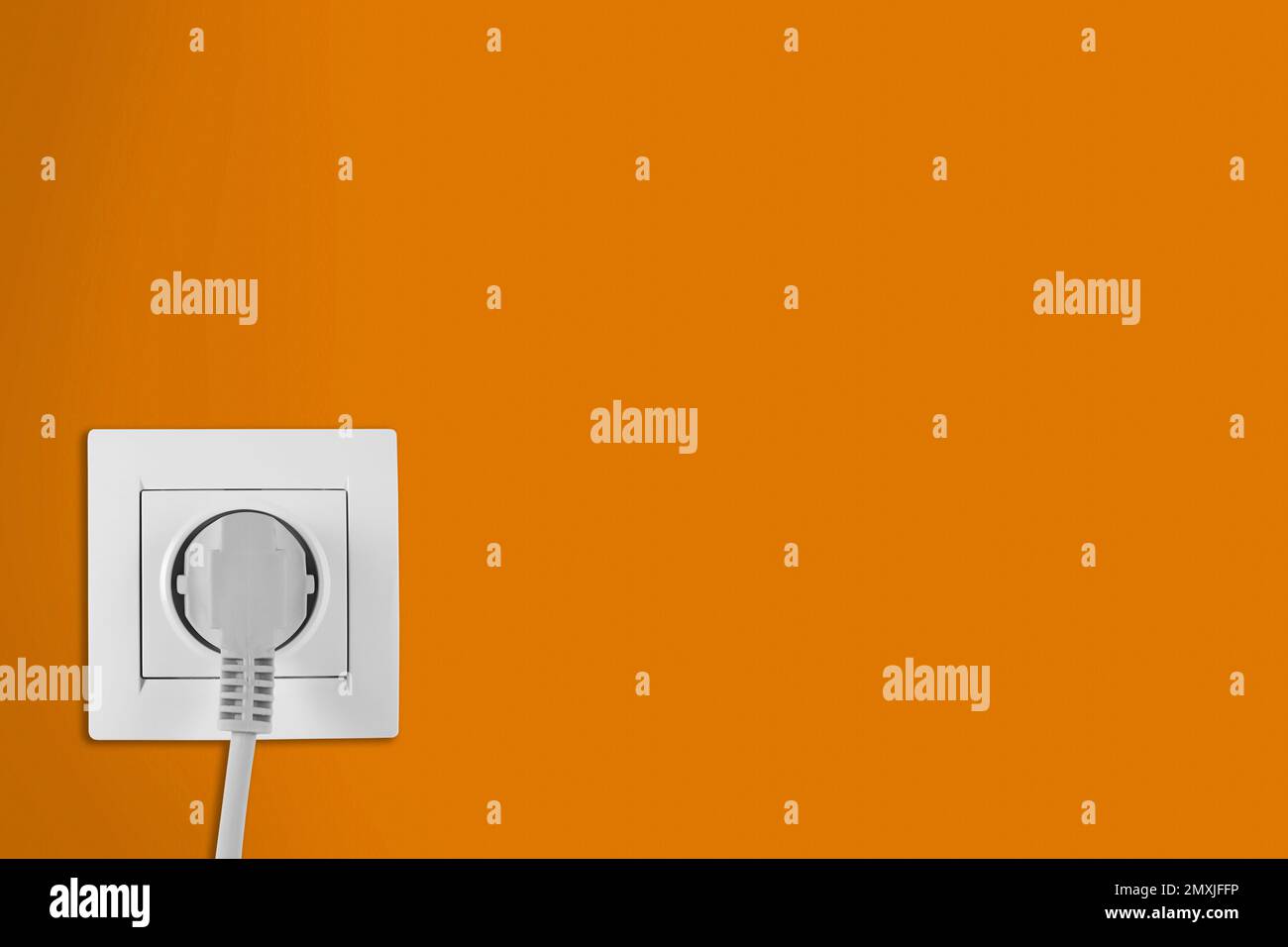 Orange wall with power socket and inserted plug, space for text