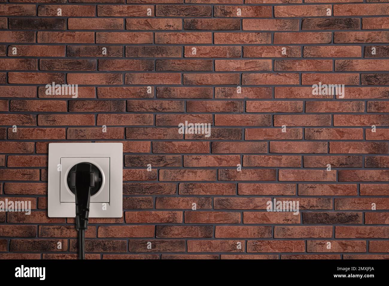 Brick wall with power socket and inserted plug, space for text