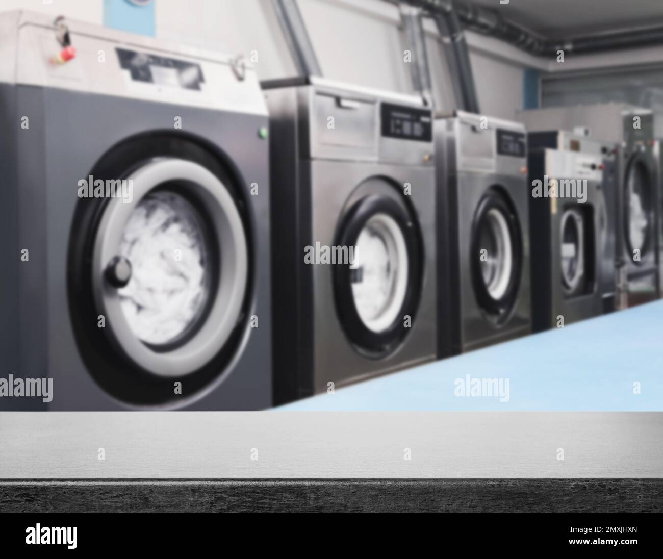 Empty grey stone surface and modern washing machines in dry-cleaning, space for text Stock Photo