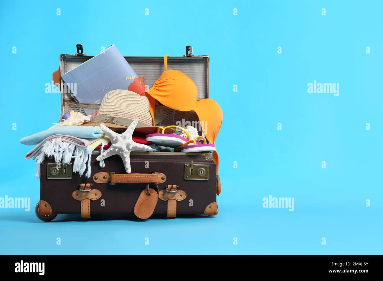 Packed vintage suitcase with different beach objects on light blue ...
