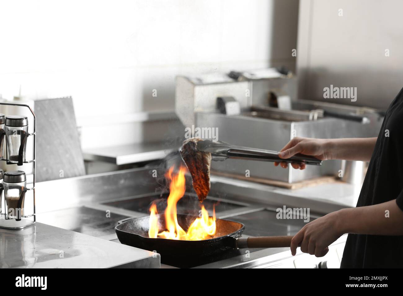 Female chef cooking meat with burning flame on stove in restaurant