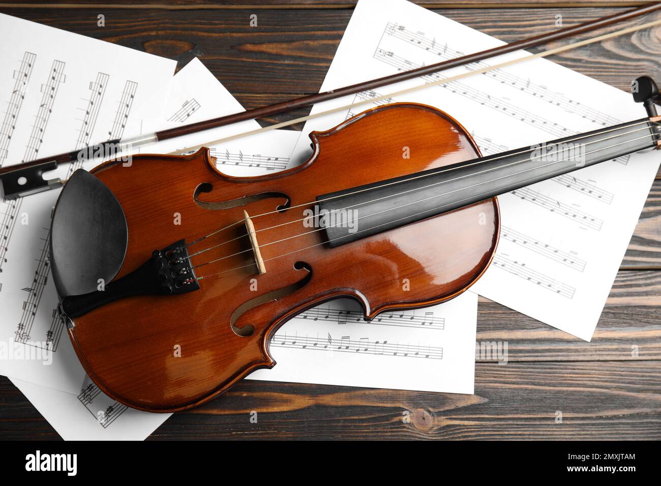 Beautiful violin, bow and note sheets on wooden table, flat lay Stock Photo