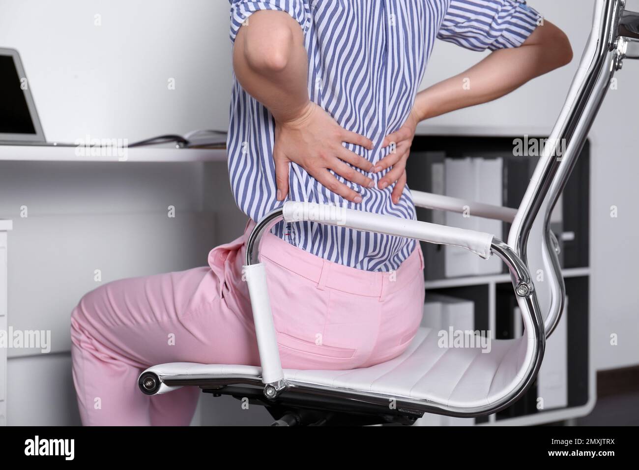 Woman with lower back pain sitting in office chair at table, closeup