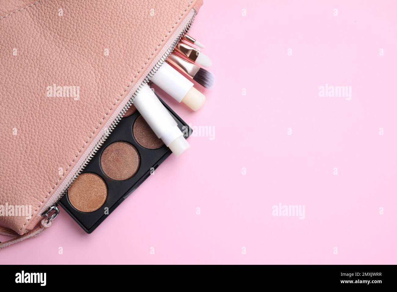 Bag with hygienic lipsticks and cosmetic products on pink background