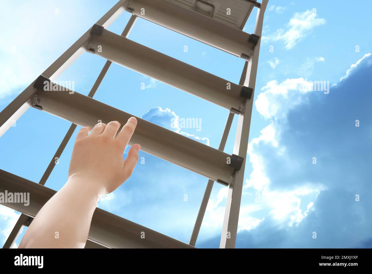 Woman climbing up stepladder against blue sky with clouds, closeup Stock Photo