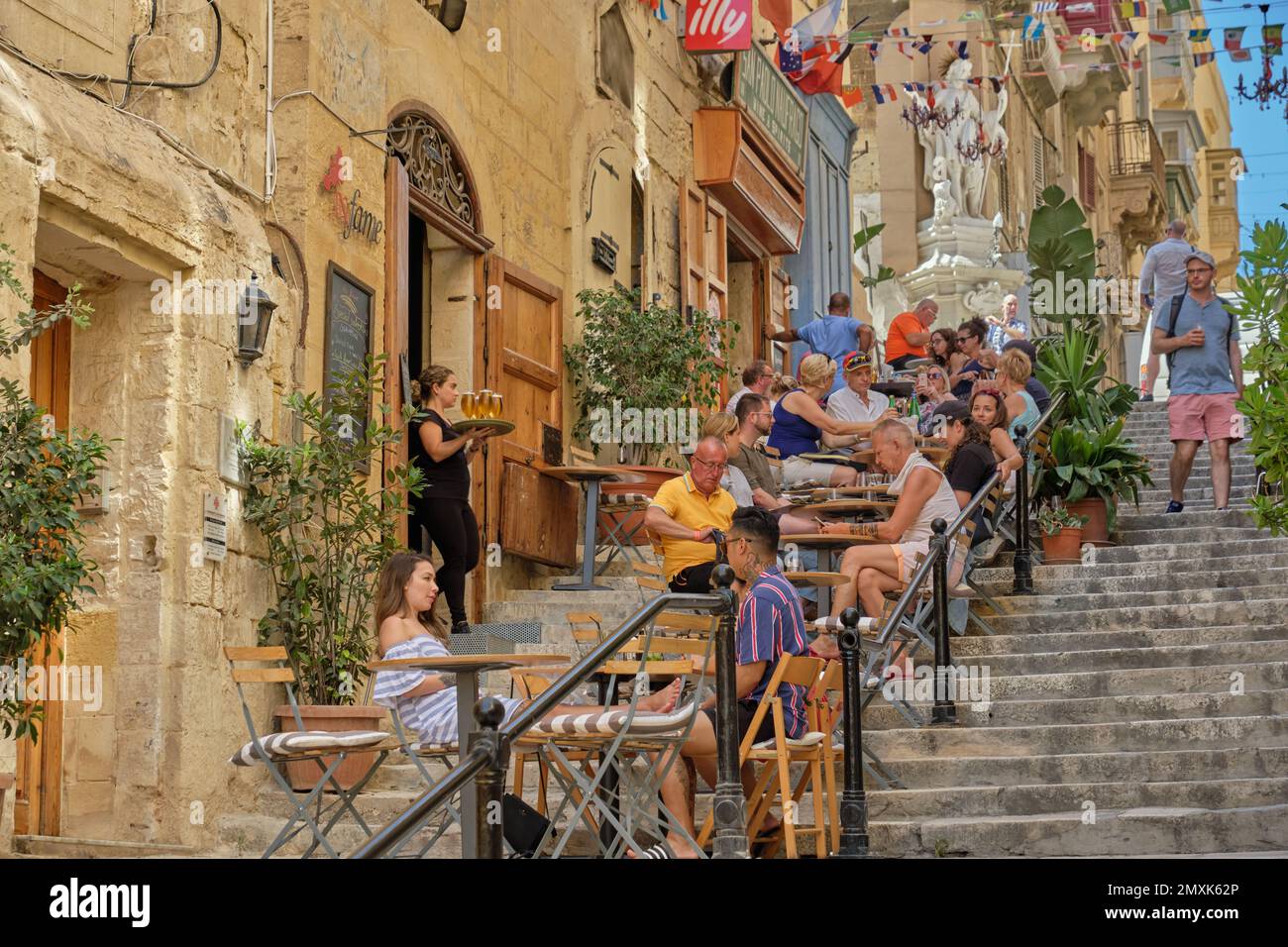 Tourists enjoy a break on the steps of the St. Lucia Street - Valletta, Malta Stock Photo