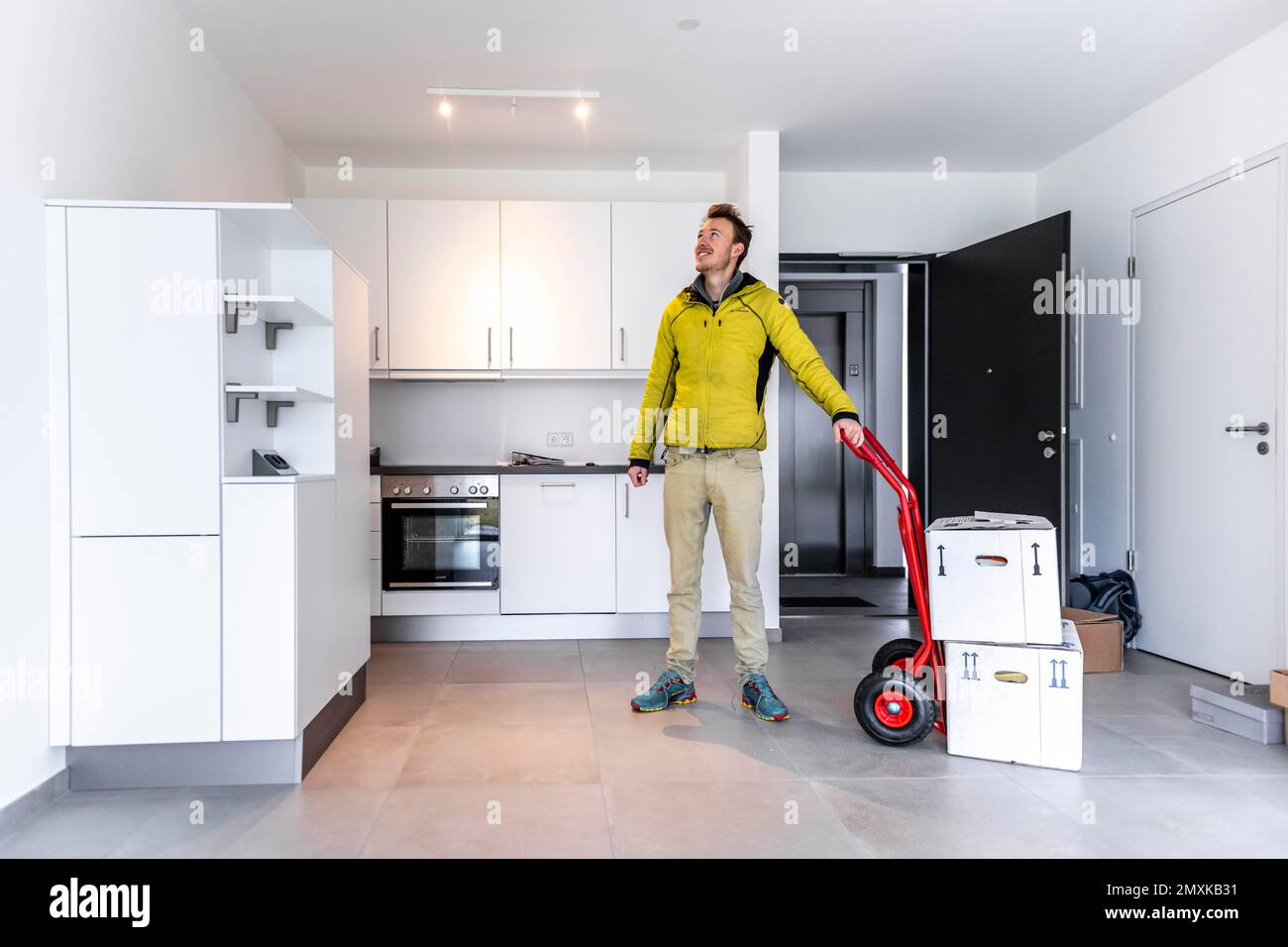 Young man with moving boxes, standing in modern kitchen of a flat, moving to a new flat, Munich, Bavaria, Germany, Europe Stock Photo