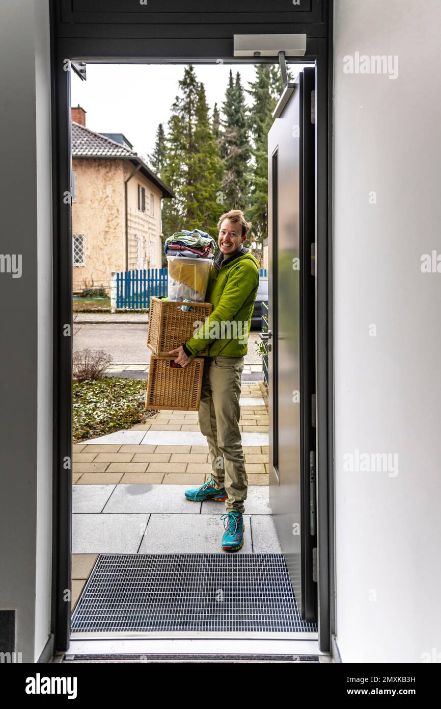 Young man carrying heavy moving boxes, view through entrance door