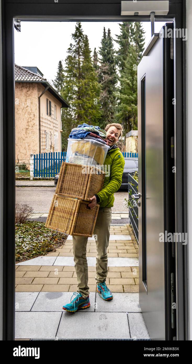 Young man carrying heavy moving boxes, view through entrance door