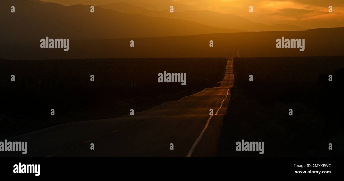 Lonely road through the desert during sunset in an orange-tinted landscape, Southern California Stock Photo