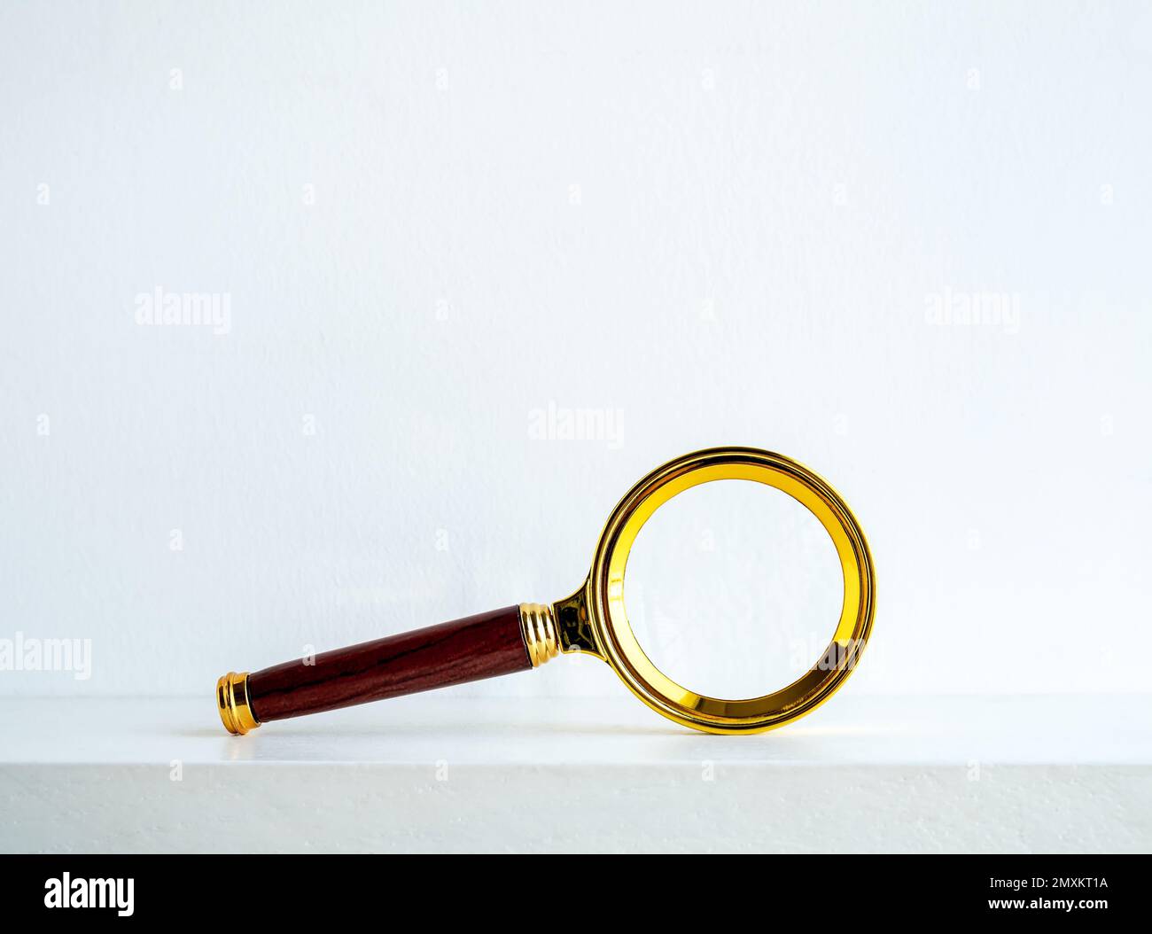 Gold magnifying glass with wood handle on white wooden shelf on white