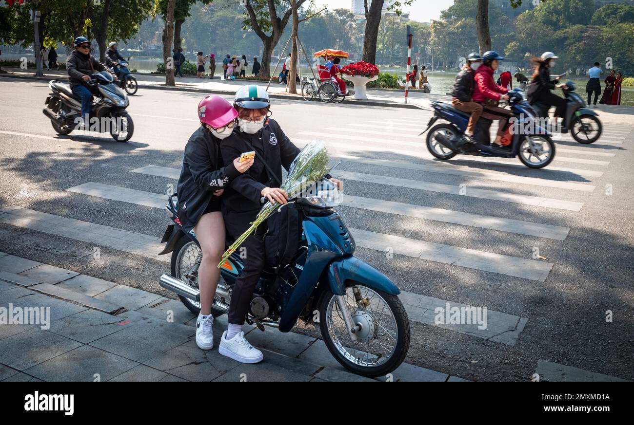 A young couple stops on their motorbike to look at a smartphone in Hanoi city centre, Vietnam. Stock Photo