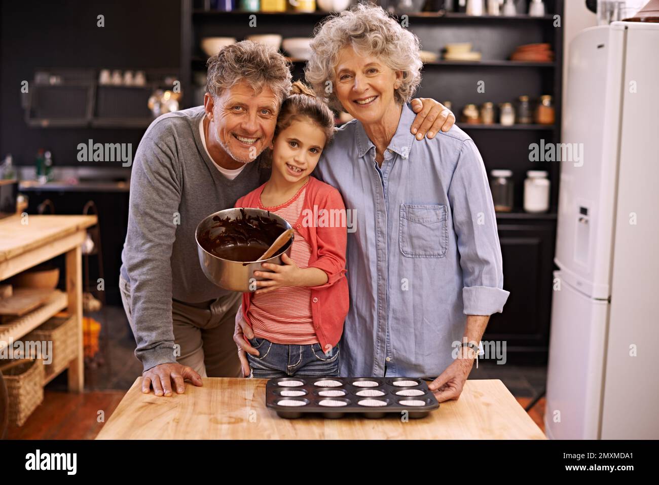 Passing down their secret family recipes. Portrait of a little girl and her grandparents making cupcakes in the kitchen. Stock Photo