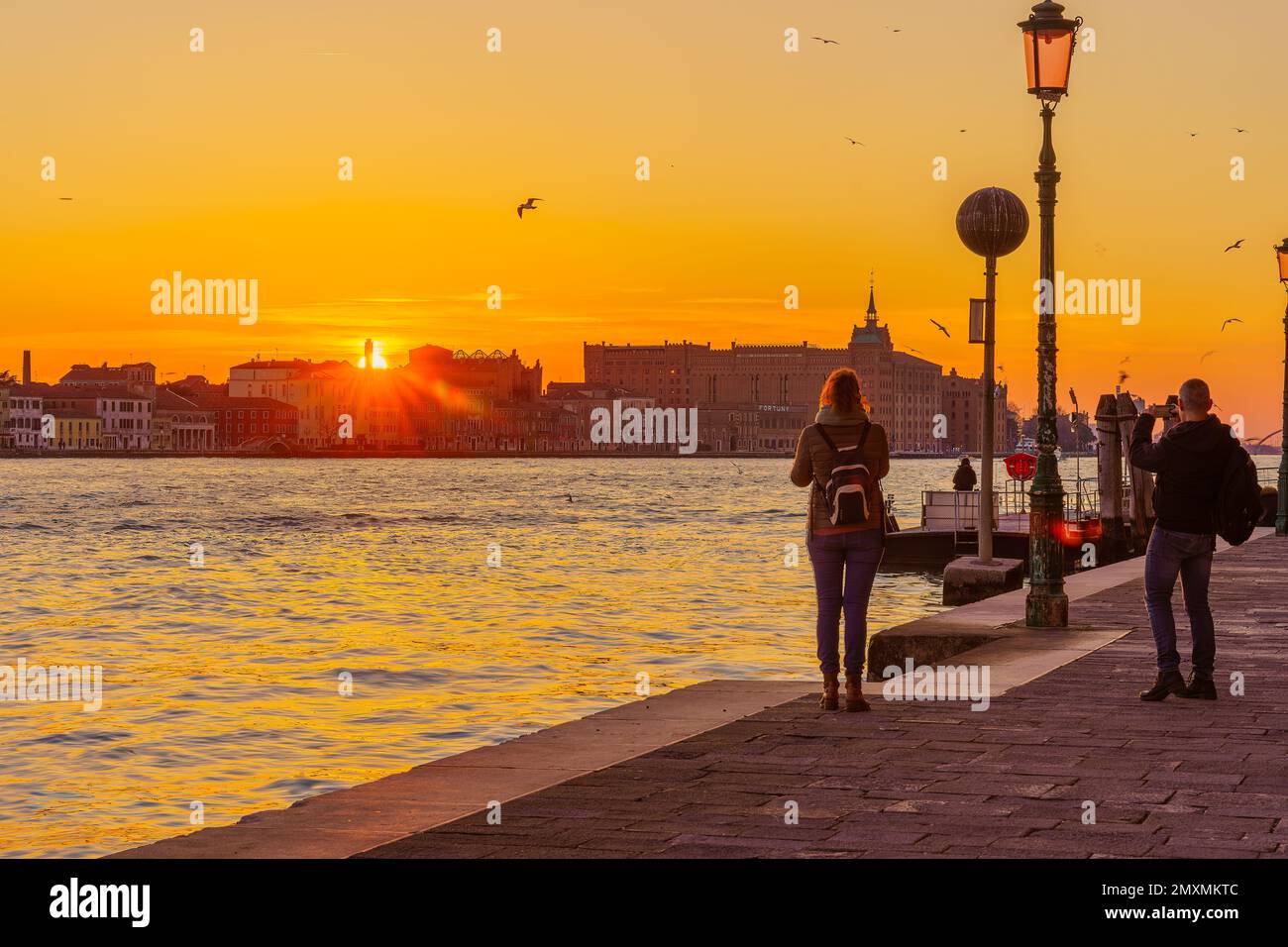 Venice, Italy - March 01, 2022: Sunset view of the Giudecca Island, with various monuments, and tourists, in Venice, Veneto, Northern Italy Stock Photo