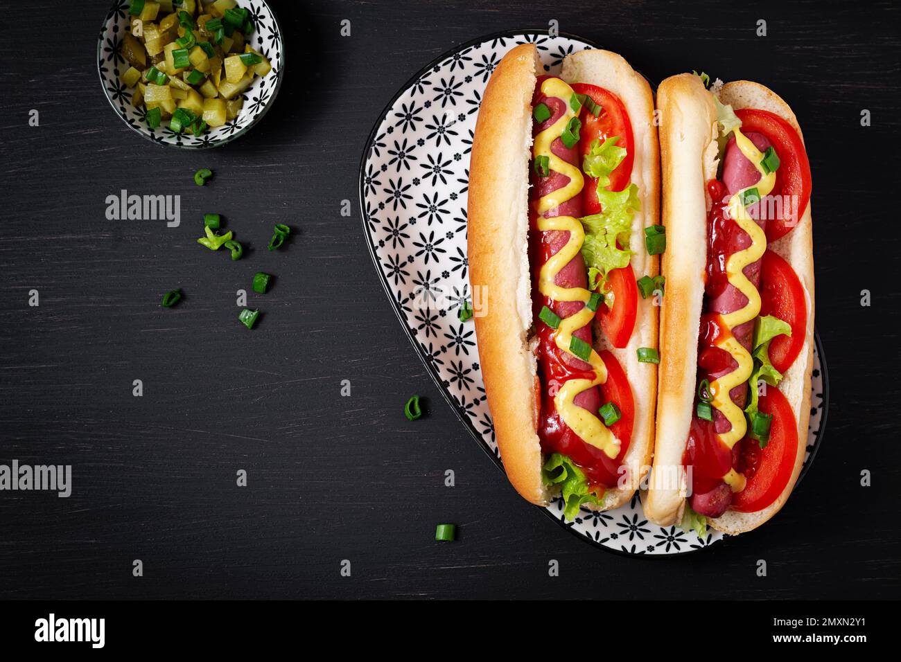 Gourmet dirty hot dog sandwich with various garnish on black slate