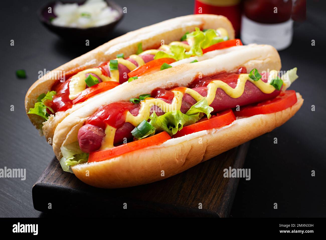 Hot dog with grilled sausage, tomato and lettuce on dark background