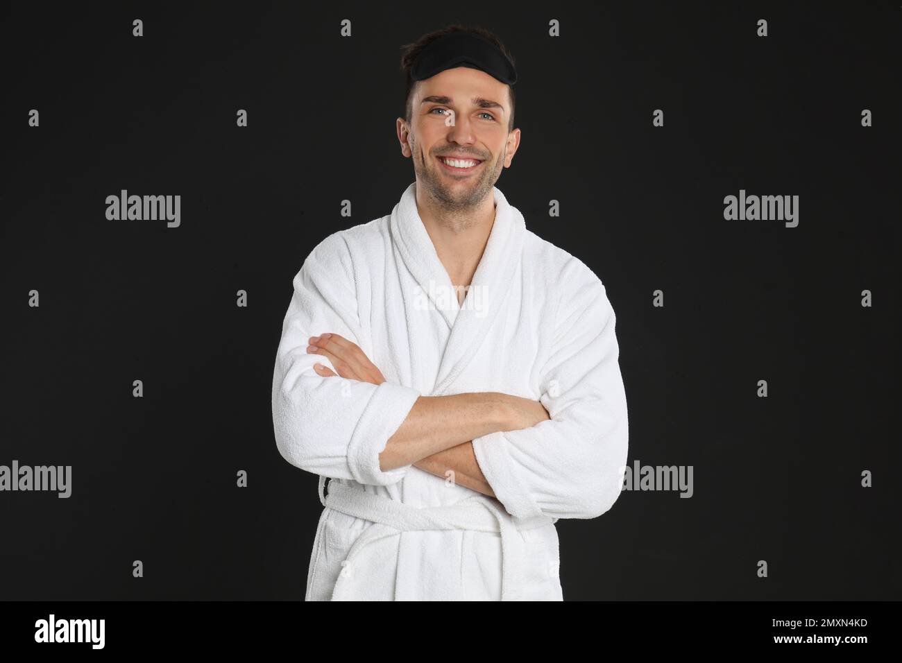 Happy young man in bathrobe and eye sleeping mask on black background Stock Photo